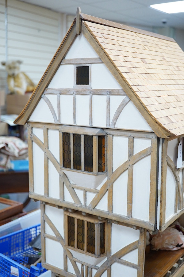 A modern doll’s house in the form of an oak framed Tudor house on three floors, with a shop on the ground floor, removable front panels on each floor and one side of the roof, with internal detailing and a good selection